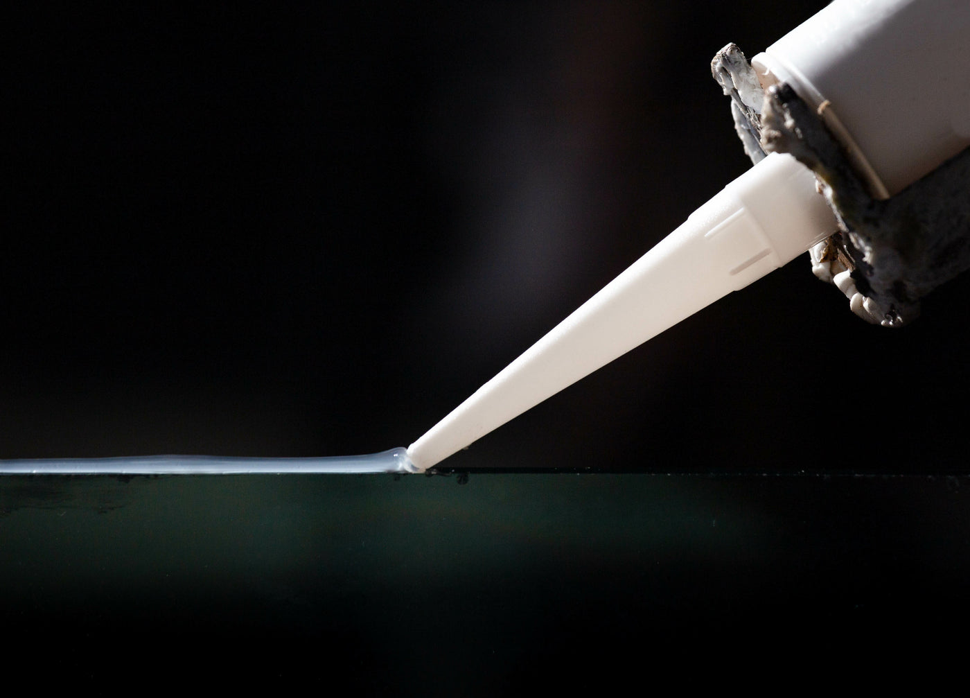 Sealant is smoothly applied to a surface against a black background using a sealant tube and applicator